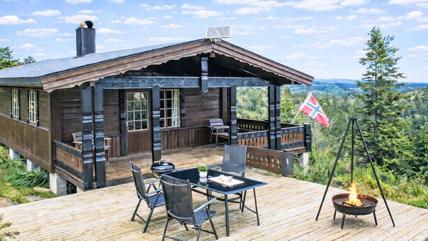 En træhytte med terrasse, udendørs møbler og et flag.