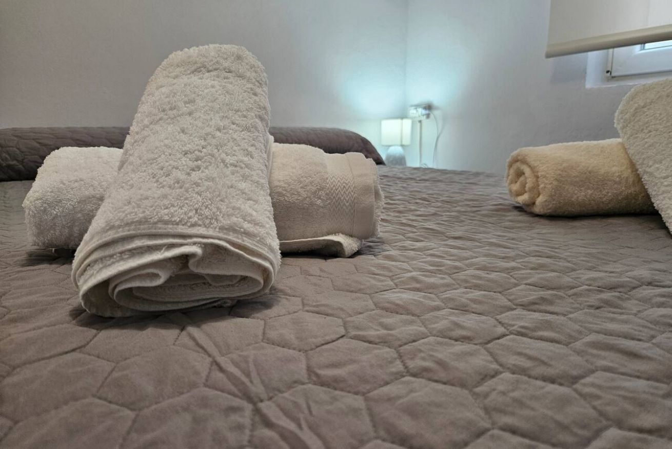 Una cama con cubrecama acolchada y toallas enrolladas.