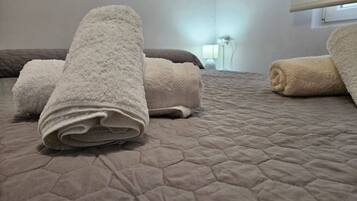 Una cama con cubrecama acolchada y toallas enrolladas.