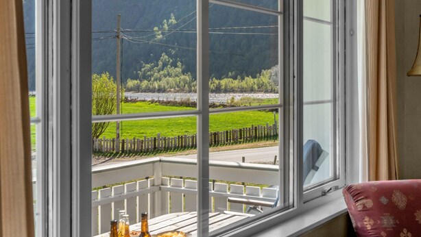 A room with a large window offering a view of a green landscape, a wooden deck, and a white railing.