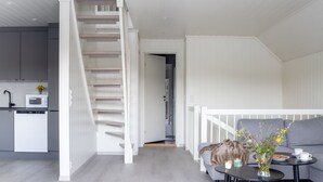 A modern interior with a staircase leading to a second floor, a kitchen area, and a seating area with a table and cushions. - Vacation home Pale by Interhome (Langevåg)