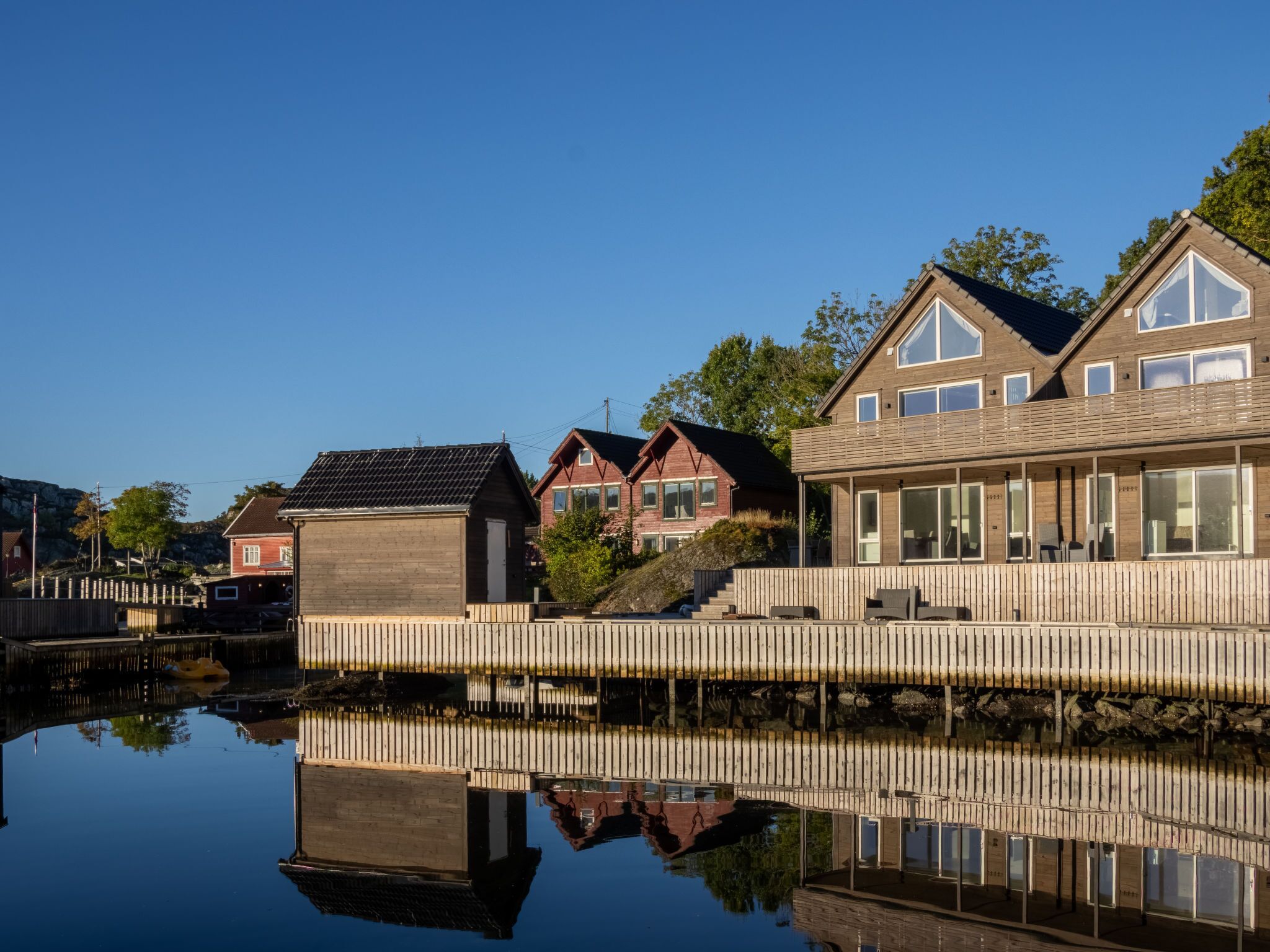 Een pand aan het water met een houten terras, een spiegelvijver en meerdere huizen met verschillende architectuurstijlen.