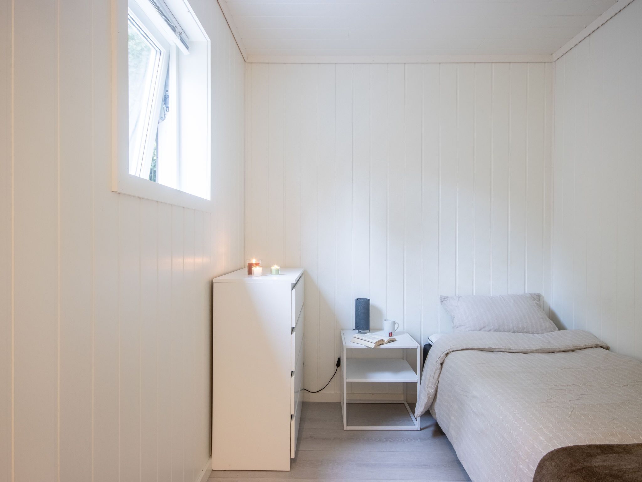 Une chambre à coucher avec un lit, une table de chevet, une commode et une fenêtre.
