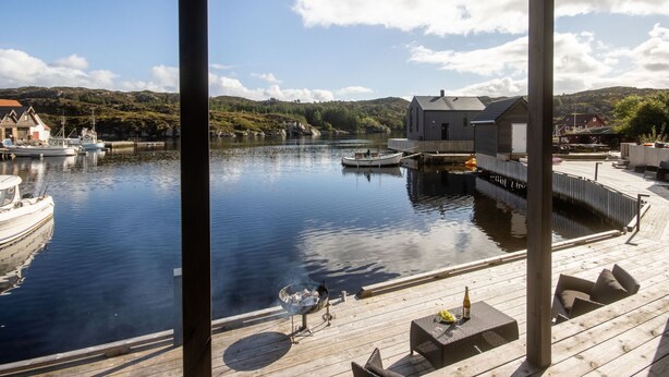 A wooden dock with a grill and seating, overlooking a calm lake with boats and houses in the background. - Vacation home Brosme by Interhome (Langevåg)
