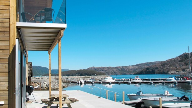 Un edificio de madera con balcón que da a un puerto deportivo con barcos y un cielo azul despejado.