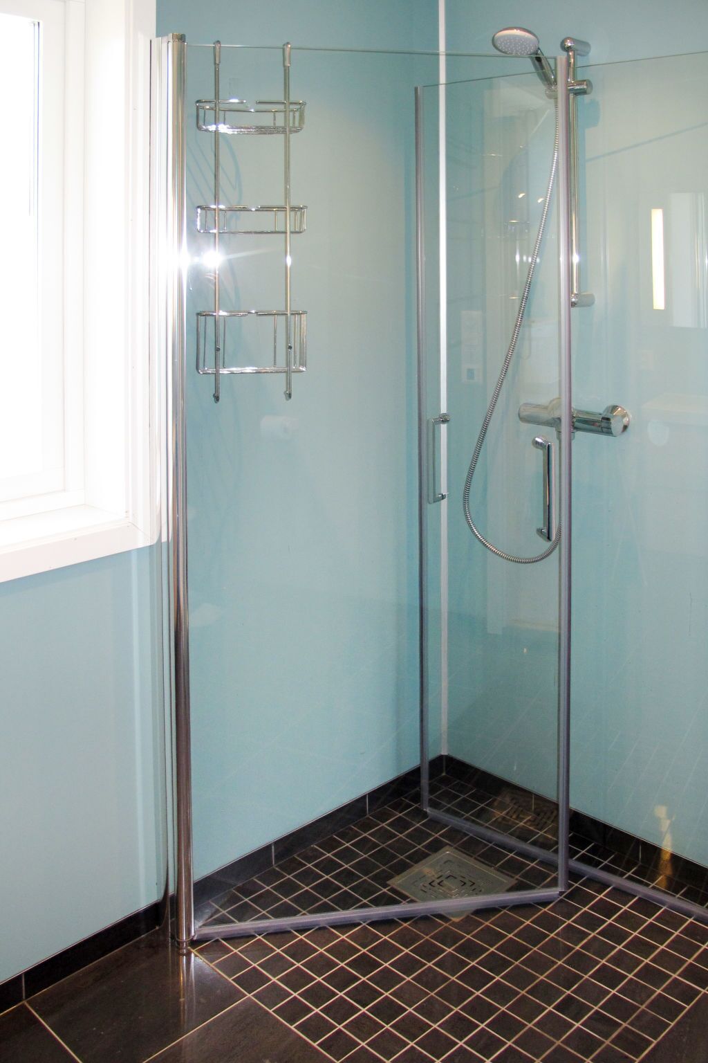 A glass-enclosed shower with chrome fixtures, a tiled floor, and a window to the left.