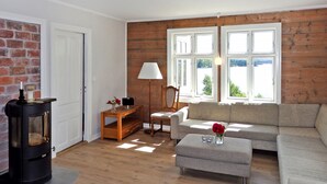 Ein gemütliches Wohnzimmer mit Kamin, einer Couch, einem Couchtisch und Blick ins Freie durch große Fenster.