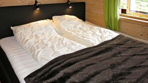 Ein Bett mit weißer Bettwäsche und einer dunklen Decke, Holzwände und ein Fenster mit Blick auf Grün.