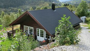 Eine Holzhütte mit dunklem Dach und einer kleinen Veranda mit Sitzgelegenheit im Freien.