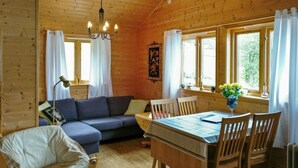 Un interior de cabaña acogedor con una mesa de comedor de madera, sillas, un sofá y una lámpara colgante.