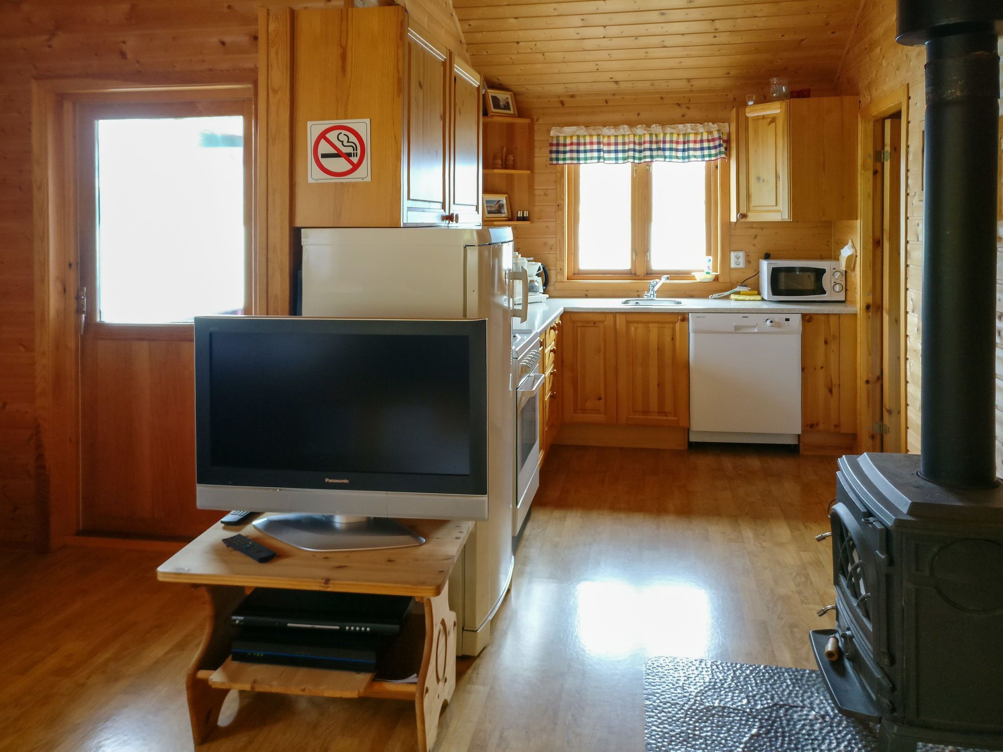 A wooden cabin interior with a television on a stand, a microwave, a sink, and a wood-burning stove.
