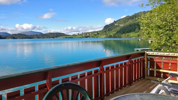 Vista al lago desde una terraza con mesa y sillas, con una masa de agua tranquila y colinas a lo lejos.