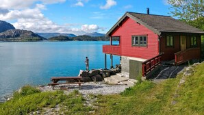 Una cabaña roja junto a un lago, con una vista despejada de las montañas al fondo.