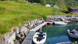 Un puerto deportivo con barcos amarrados, una costa rocosa y casas al fondo.