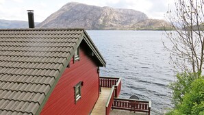 Un edificio rojo con techo de tejas que da vista a una masa de agua y una montaña al fondo.
