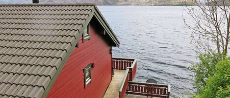 A red building with a tiled roof overlooking a body of water and a mountain in the background.
