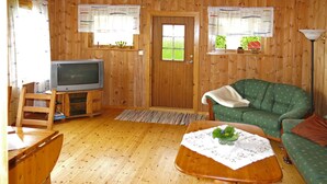 A wooden-paneled room with a television, a green sofa, a wooden table with a floral tablecloth, and a door with a window. - Vacation home Nanna by Interhome (Risnes)