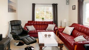 Ein Wohnzimmer mit einem roten Ledersofa, einem schwarzen Ledersessel, einem Holztisch und einem Kamin.