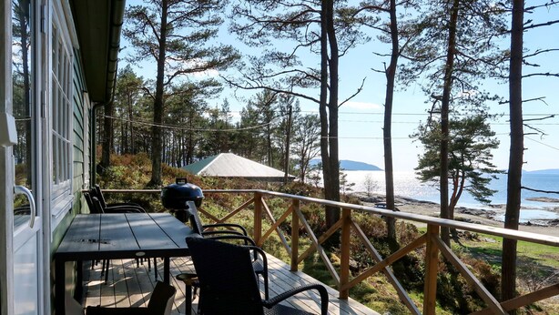 Eine Holzterrasse mit Tisch und Stühlen mit Blick auf Strand und Wald.