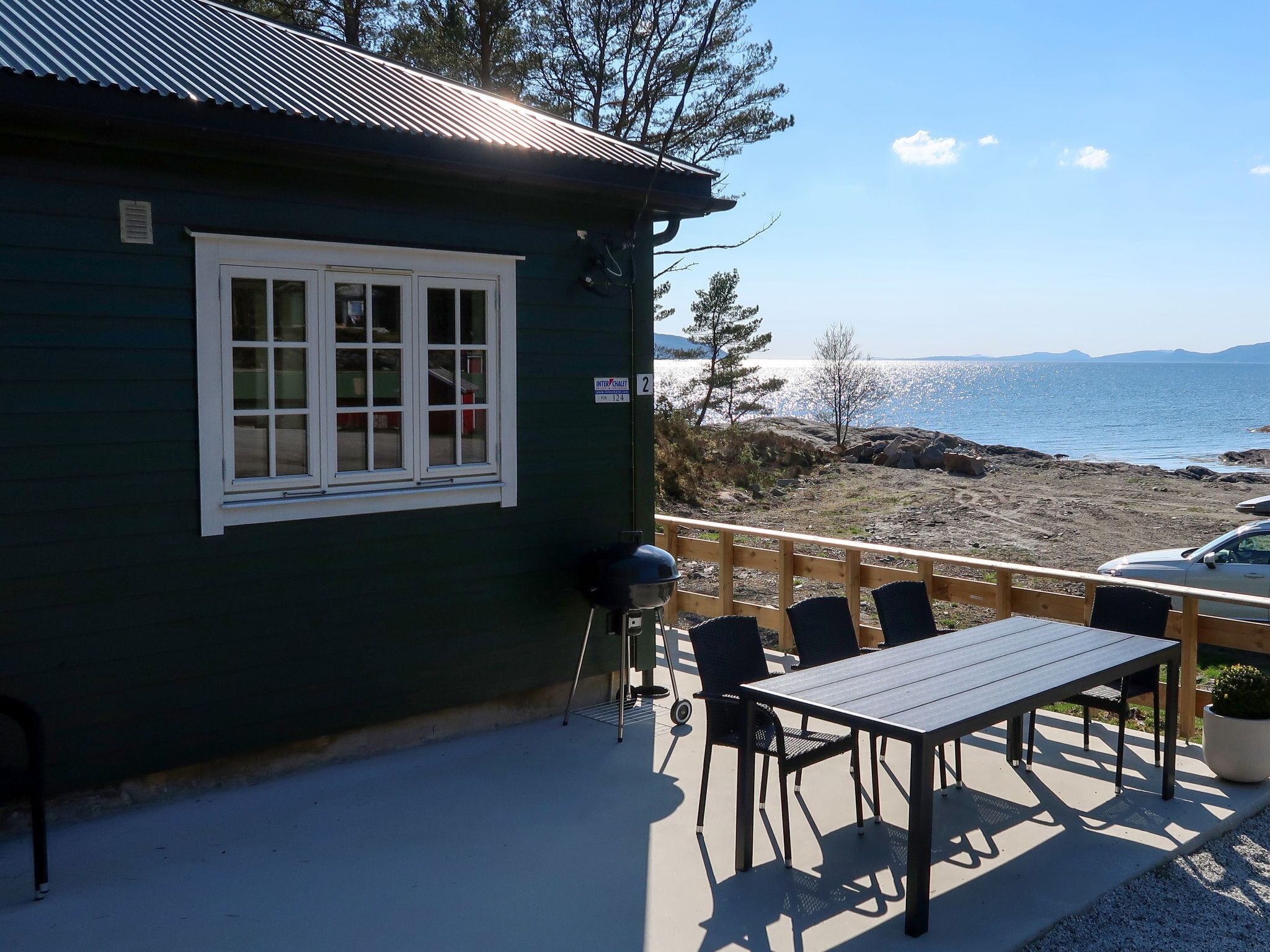 A small building with a window and a deck overlooking a rocky shoreline and water.