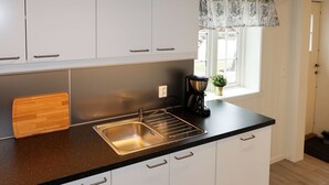 Una cocina moderna con armarios blancos, encimera negra, pileta de acero inoxidable y cafetera.