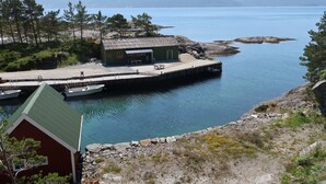 Una cabaña junto al lago con un muelle que se adentra en el agua, rodeada de árboles y terreno rocoso.