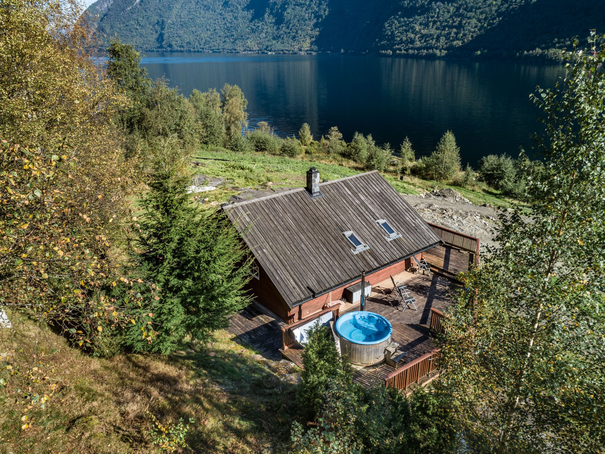 A cabin with a sloped roof, a hot tub, and a deck overlooking a lake.