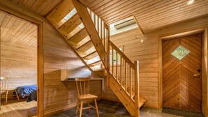 Een houten interieur met een trap, een bed en een deur met een ruitvormig raam.