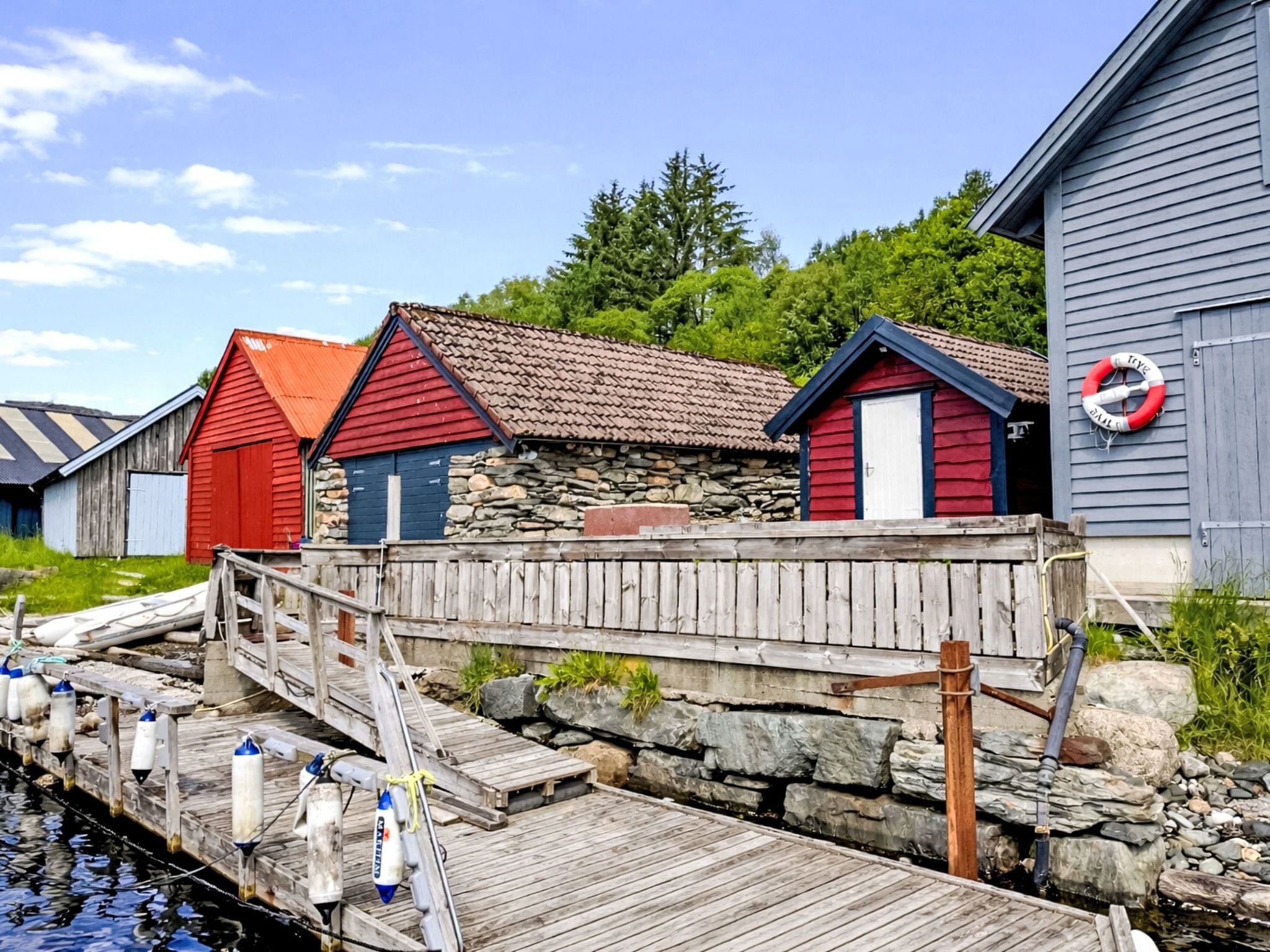 A wooden dock leading to a row of small, colorful cabins with stone walls and metal roofs.