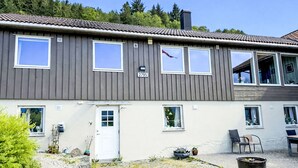 Ein zweistöckiges Gebäude mit grauer Fassade, mehreren Fenstern, einer Tür und einem kleinen Garten mit Gartenmöbeln.