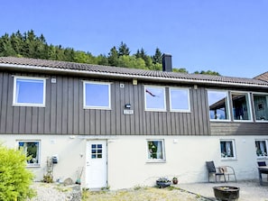 A two-story building with a grey facade, multiple windows, a door, and a small garden area with outdoor furniture. - Mjellhaugen by Interhome (Vevring)