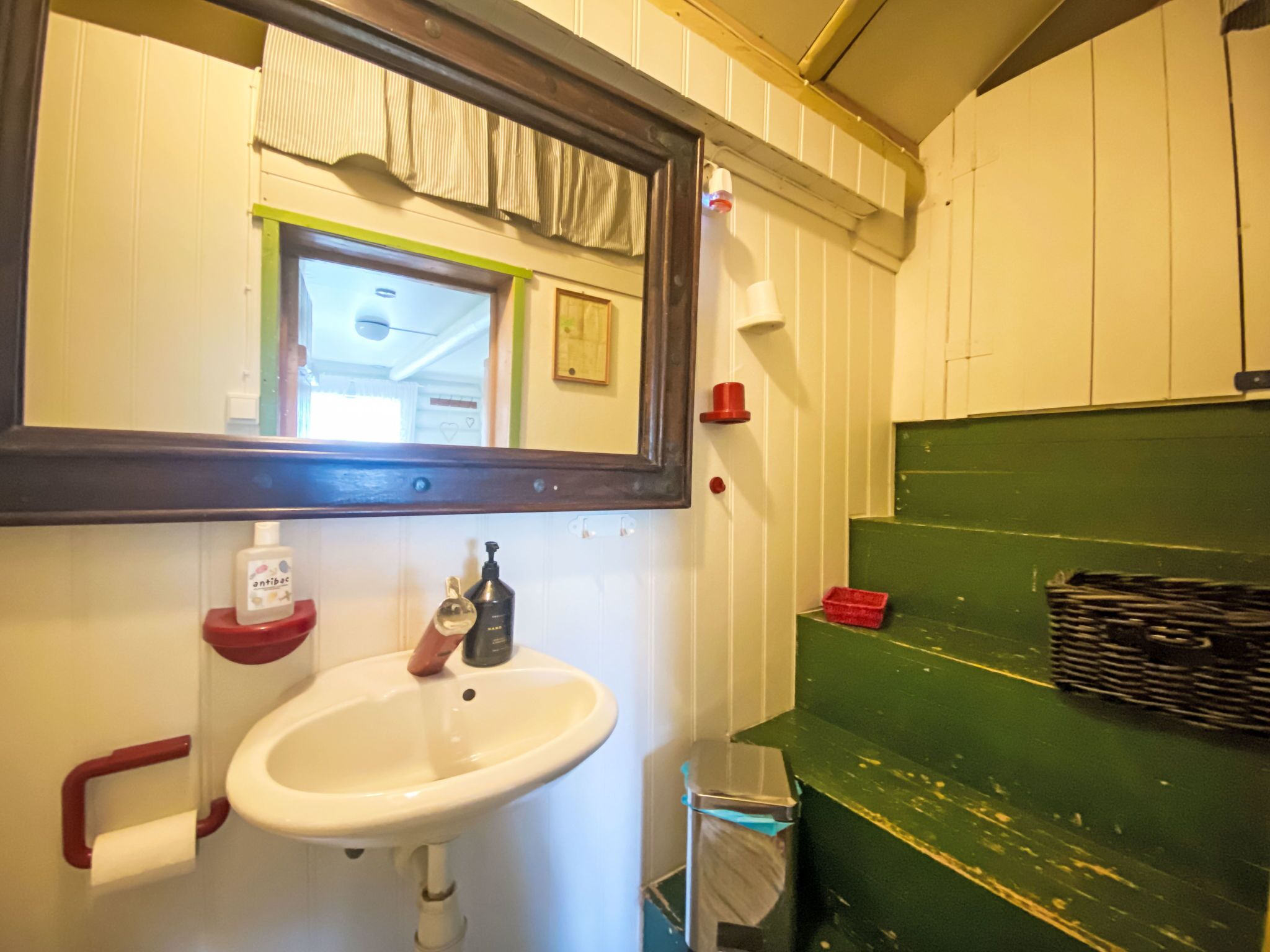 A bathroom with a white sink, a mirror, a red soap dispenser, and a green shelf.