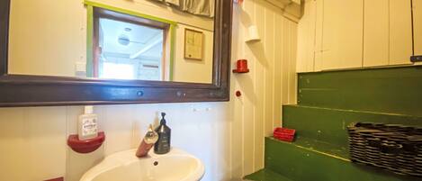 A bathroom with a white sink, a mirror, a red soap dispenser, and a green shelf.
