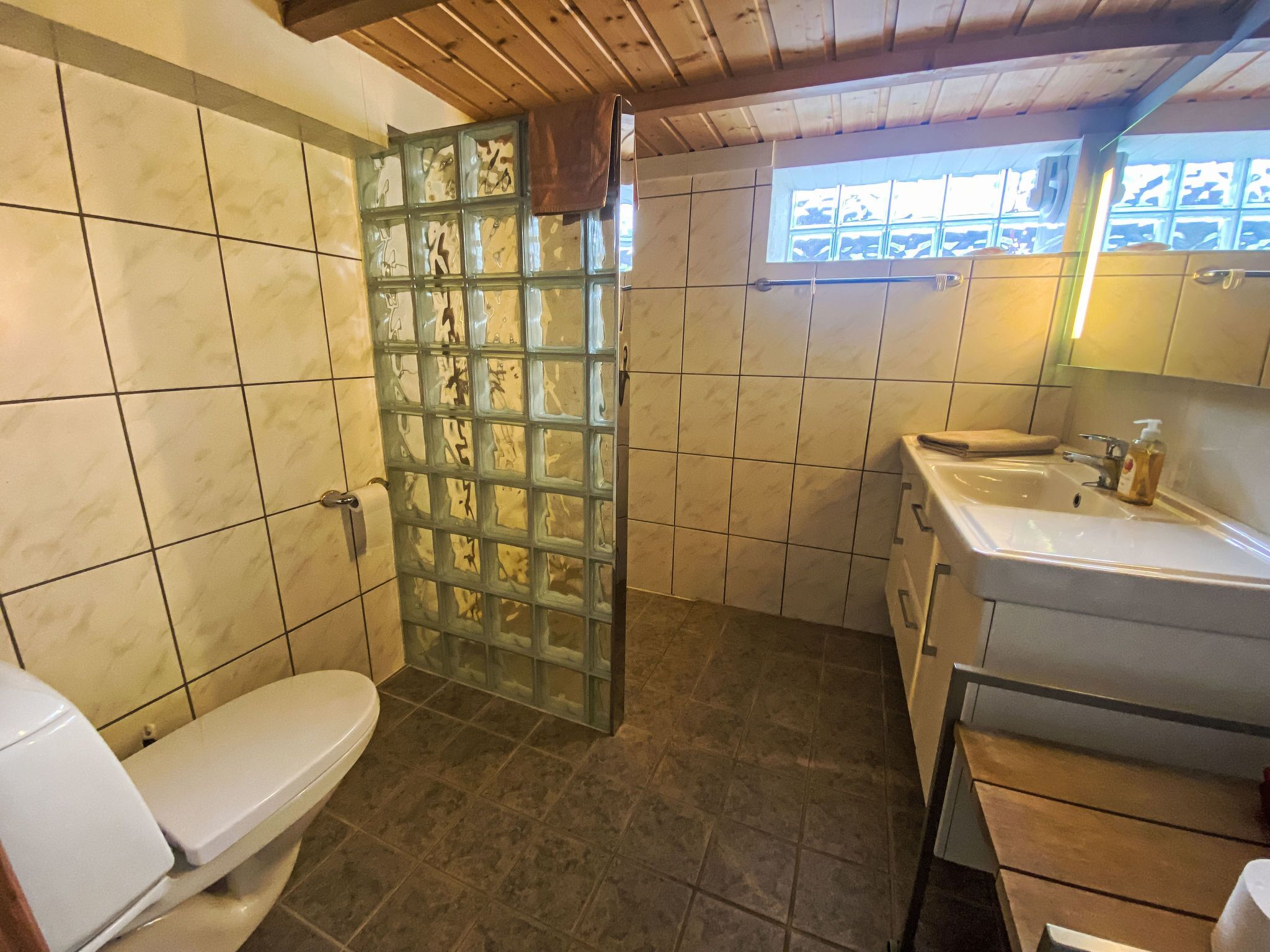 Een badkamer met toilet, glazen douchecabine, wastafel en raam.