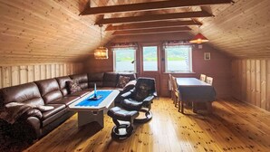 A cozy cabin interior with a brown leather sofa, a small table with a blue placemat, a leather armchair, and a dining table with chairs. - Naustet by Interhome (Åheim)