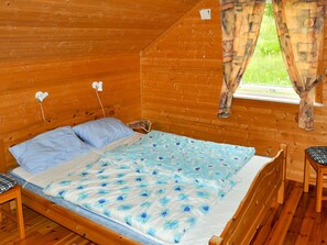 A wooden cabin room with a bed, a window with curtains, and a small table.