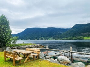 A lakeside picnic area with a wooden bench and table, surrounded by rocks and a dock.