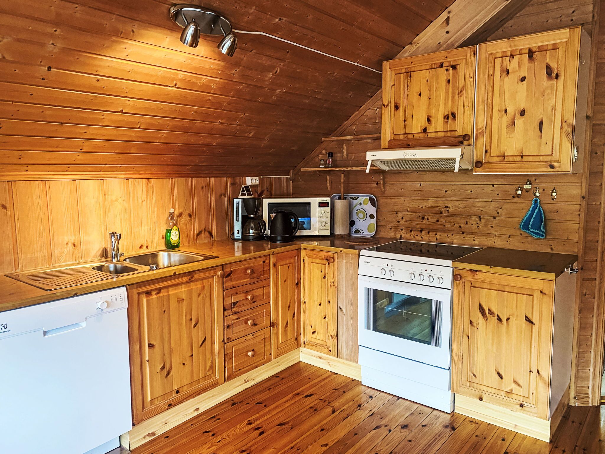 A wooden cabin-style kitchen with a dishwasher, stove, microwave, and coffee maker.