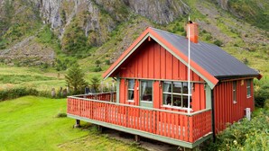 Una cabaña roja de madera con un balcón, con montañas al fondo.