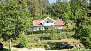 Una casa amb teulada vermella, envoltada d'arbres i una massa d'aigua.