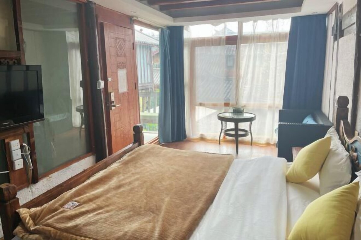 A bedroom with a bed, a television, a small table, and a view of the outside.