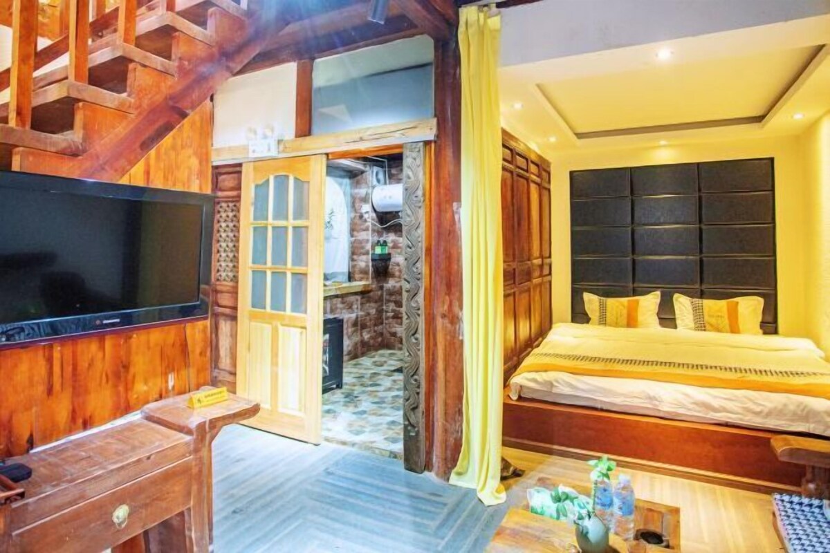 A hotel room with a wooden staircase, a large bed with yellow bedding, a television, and a small table with a vase of flowers.