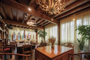 A wooden dining area with a large table and chairs, a chandelier, and curtains.