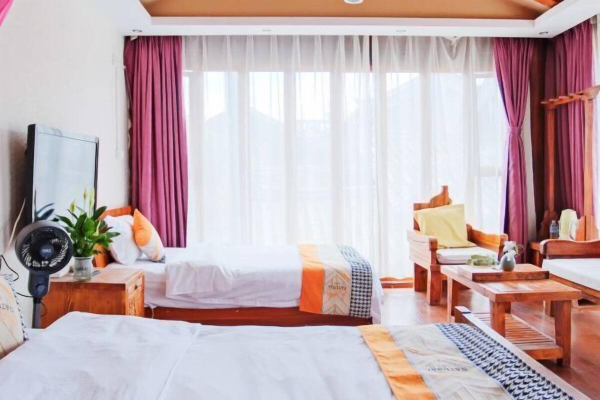 A hotel room with two beds, a wooden sofa, a small table, and a fan.