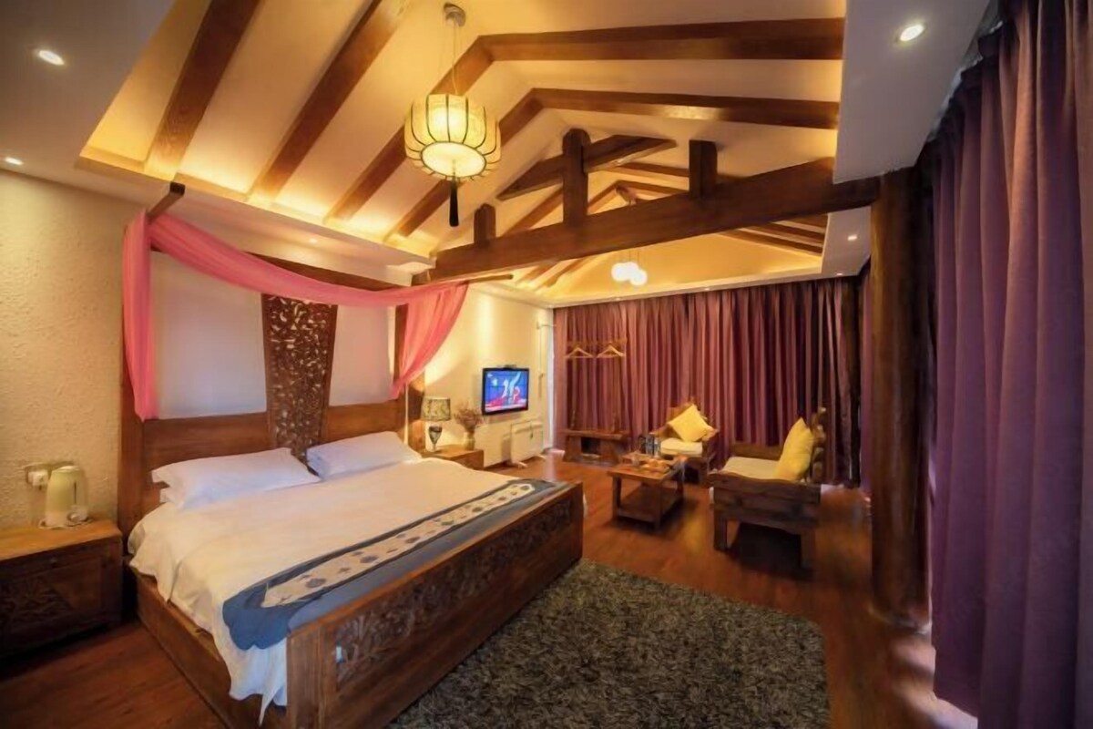 A bedroom with a large bed, a television, a wooden coffee table, and a seating area with a chair and a sofa.