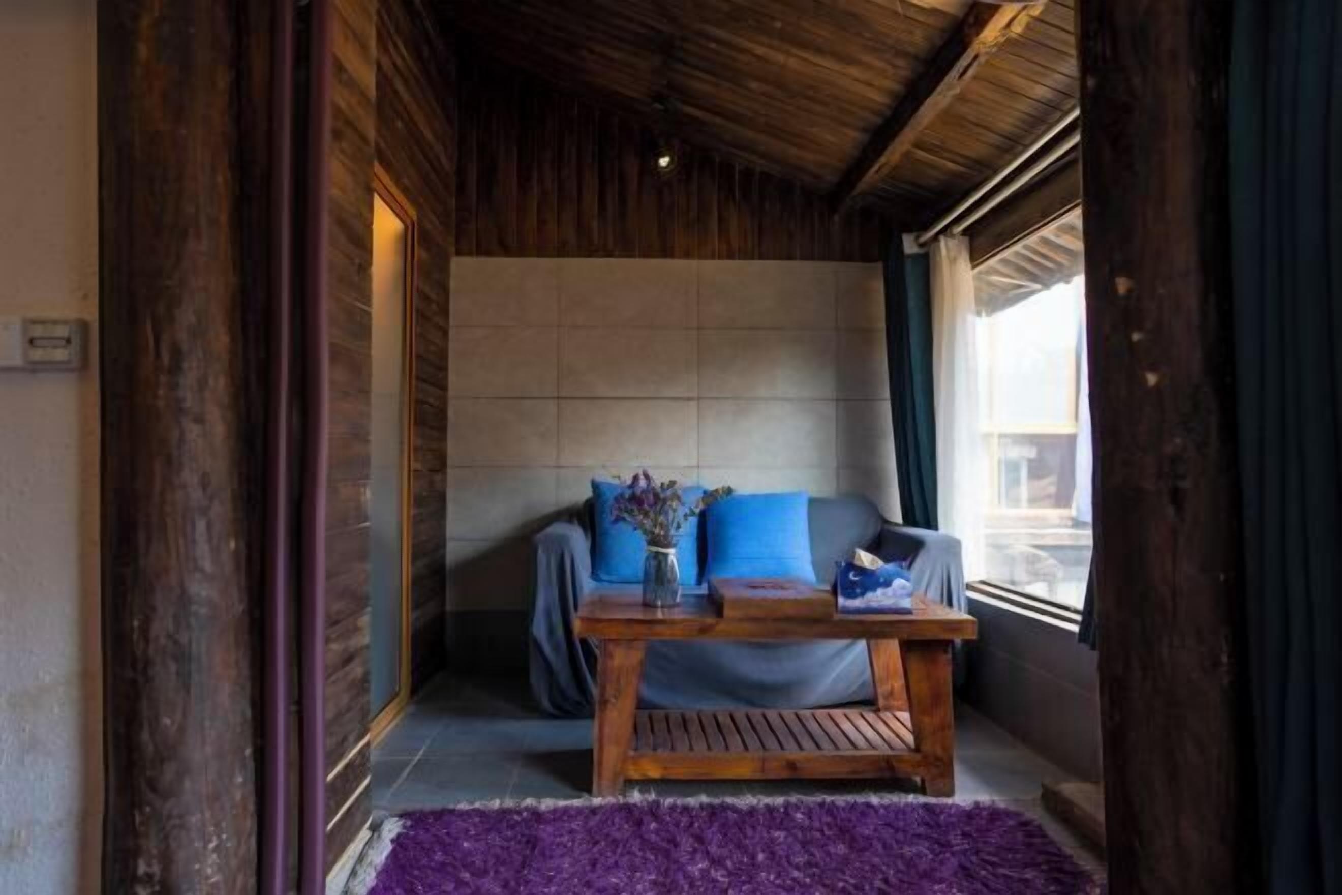 A cozy room with a wooden ceiling, a sofa with blue cushions, a small wooden table, and a purple rug.