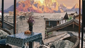 A traditional Chinese courtyard with stone walls, a table with a blue tablecloth, and a view of mountains. - Lijiang Yuanshu Inn (Shuhe Ancient Town Branch) (Lijiang)