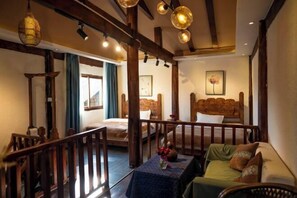 A cozy room with a bed, a sofa, and a table with a vase. There are wooden beams and a chandelier.