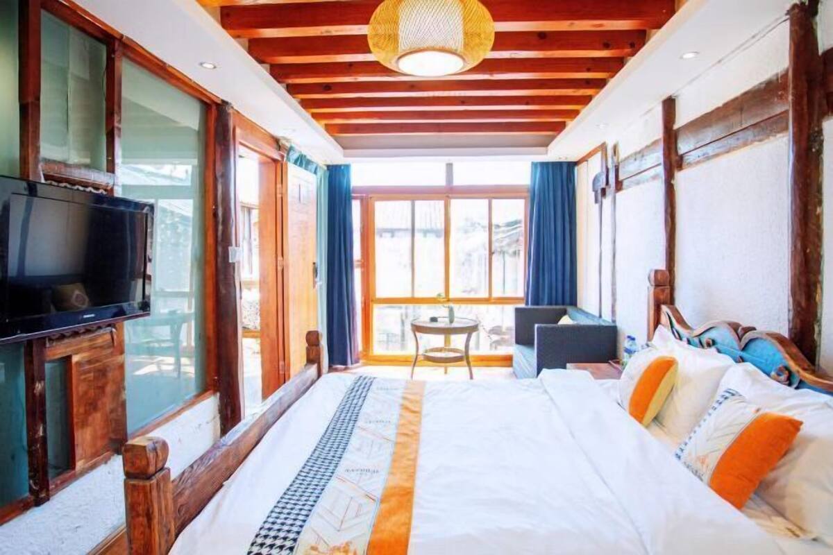 A bedroom with a bed, a television, a desk, and a window.