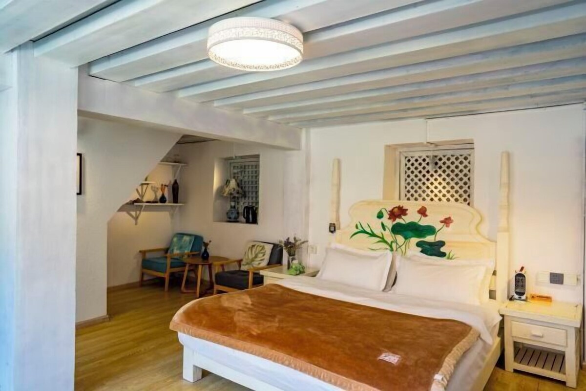 A bedroom with a bed, a nightstand, a chair, and a wooden floor.